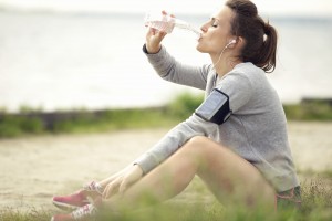 Tired female jogger sitting on the grass and drinking bottled water